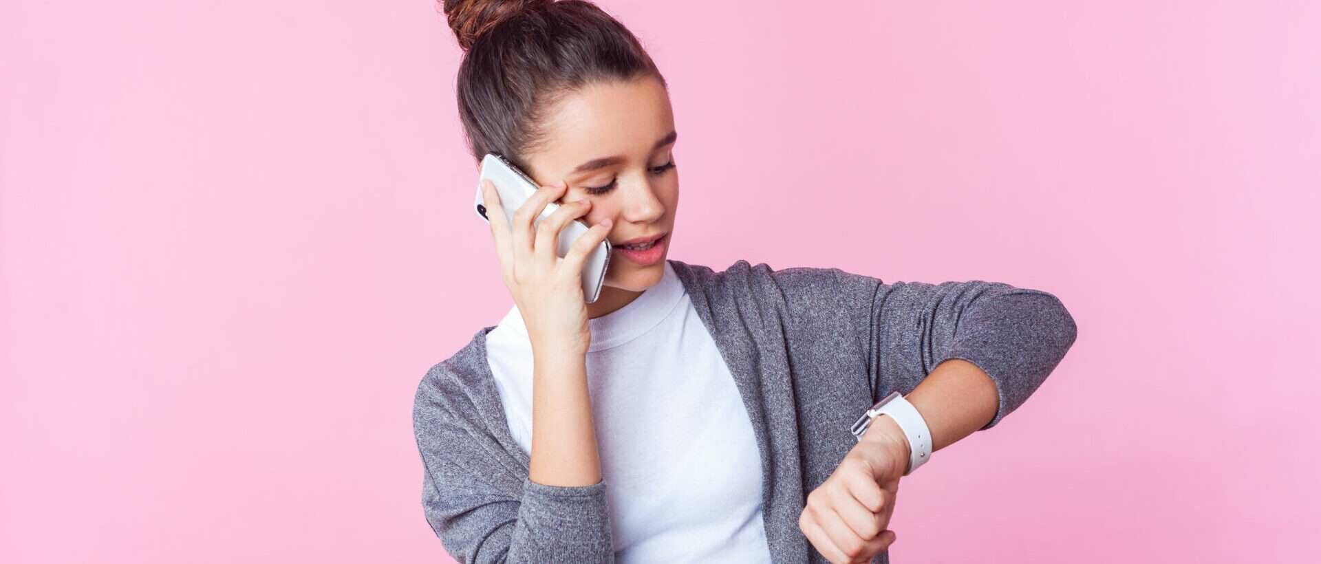 ピンクの背景に時計を見つめる若い女性。