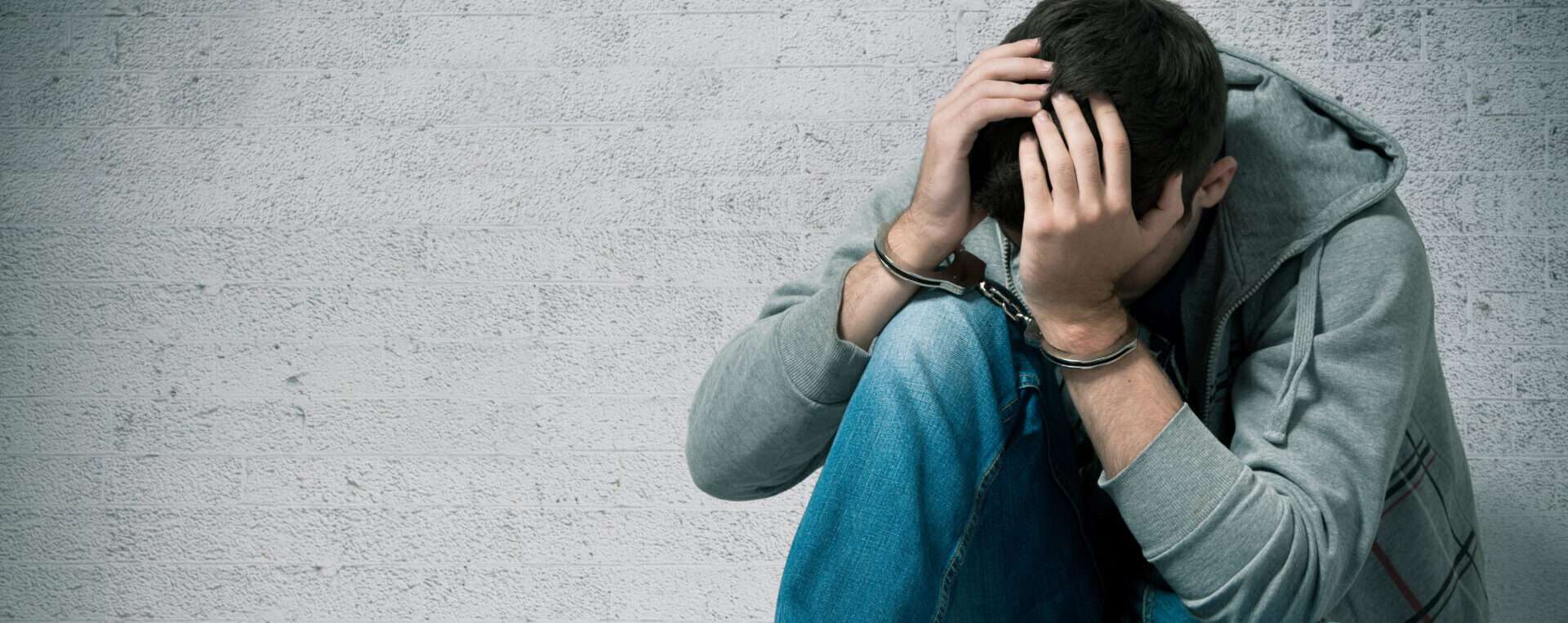 男性が頭に手を当てて床に座っており、苦しそうな表情をしている。