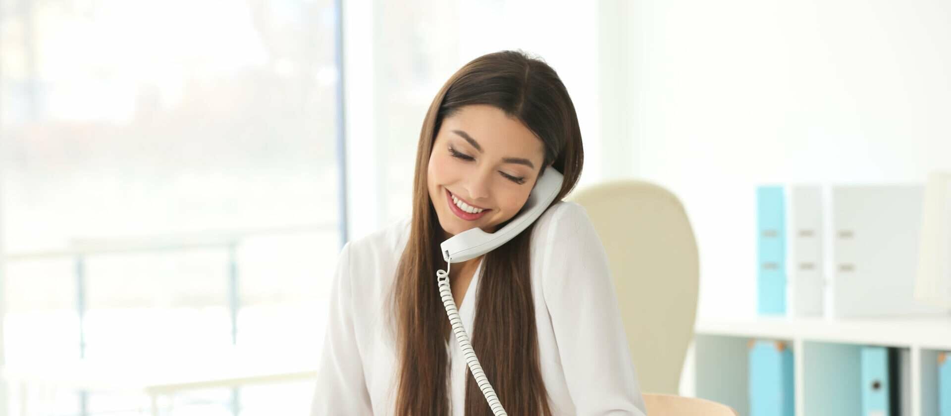 女性が机に座りながら電話で話しています。