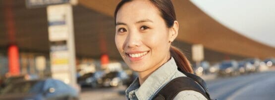 バックパックを背負ったアジア系の若い女性が交通量の多い通りで英語で会話しています。