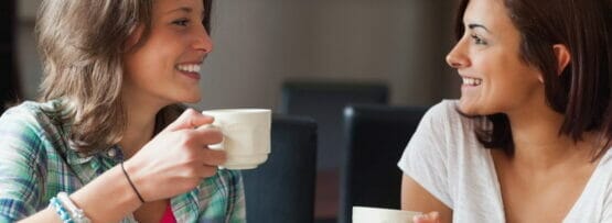 テーブルに座ってコーヒーマグを飲みながら英会話をしている 2 人の女性。