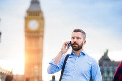 ロンドンのビッグベンの前で、男性が電話で英語を話しながら英会話をしている。