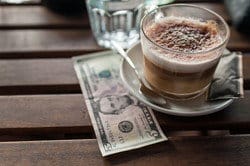 コーヒーのカップの上にドル紙幣が乗っており、カフェでの英会話の練習に最適です。