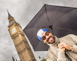 ビッグベンの前で傘を差しながら英会話をする男性。