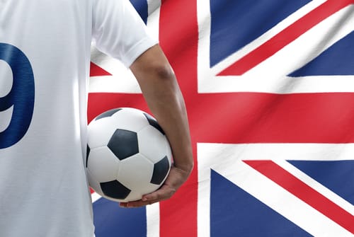 英国国旗の前でサッカー ボールを持ち、他の人と英会話をしている男性。