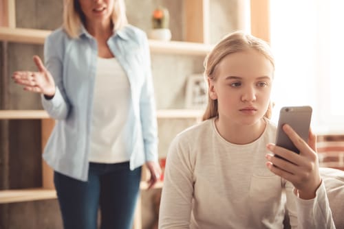 若い女の子が携帯電話に夢中になっている間、母親はそれを見つめています。