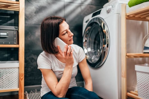 洗濯機の前に立ちながら電話で英会話をする女性。