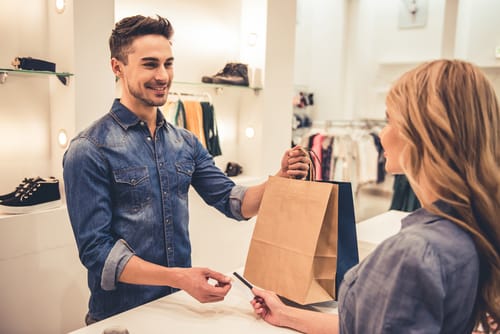 店内で男性が英語で会話しながら女性に買い物袋を渡している。