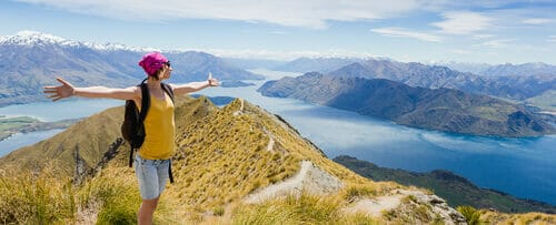 山の頂上に立って両手を広げ、英会話に取り組み、英語スキルを練習している女性。