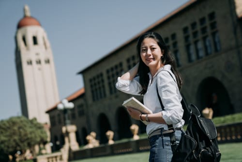 時計塔のある建物の前に立って英会話の練習をしている若い女性。