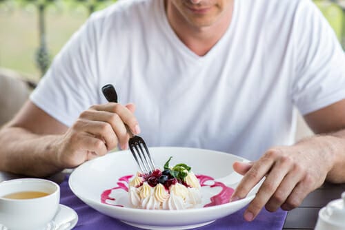 おいしいデザートをフォークで味わいながら英会話をする男性。