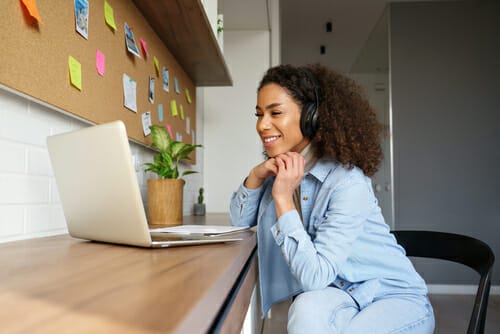 ヘッドフォンを着けた女性がノートパソコンを持って机に座っています。日本語。