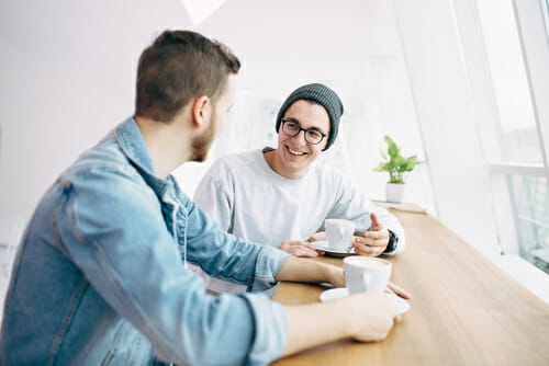 テーブルに座ってコーヒーを飲みながら英語で話している二人の男性。