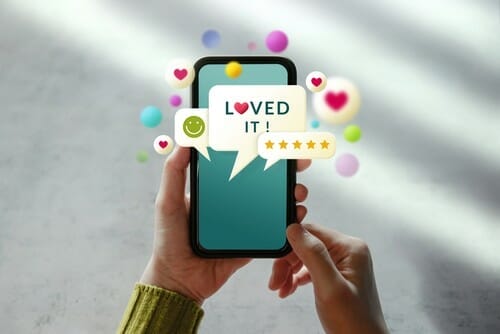 英語で「loved it」と書かれたスマートフォンを掲げる女性。 英語で「loved it」と書かれたスマートフォンを掲げる女性。
