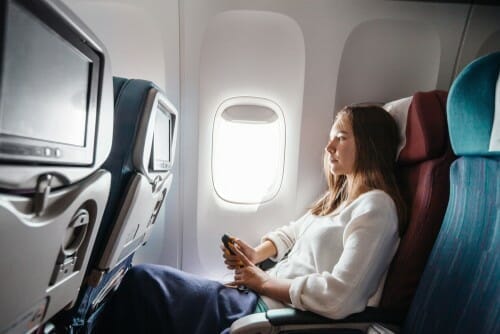 飛行機の中で座って携帯電話を見ている女性。日本語。