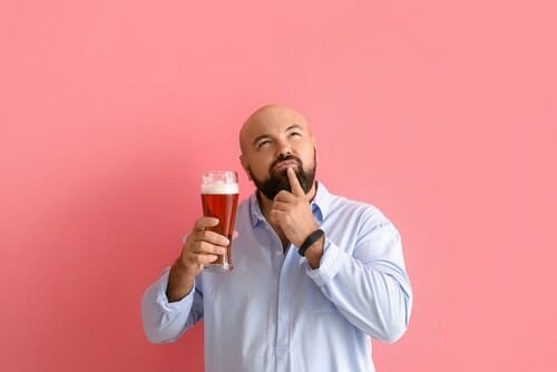 ピンクの背景の前でビールのグラスを持っているハゲの男性。