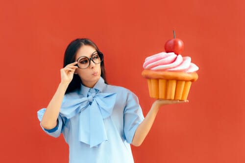 女性は赤い背景の前でカップケーキを持っています。