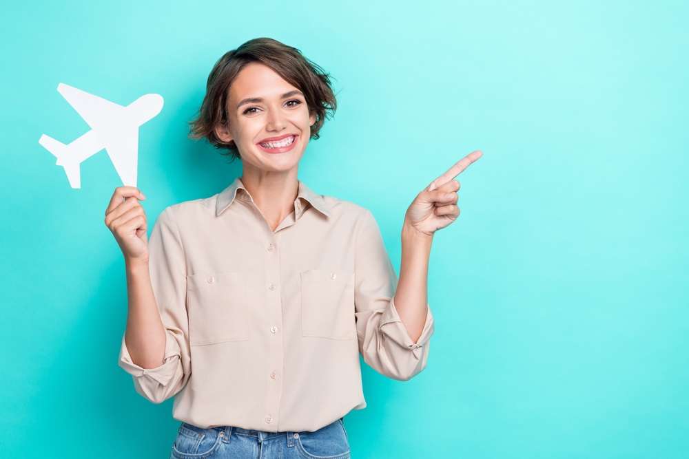 紙飛行機を持ち、もう片方の手で英語の本を持って紙飛行機を指している女性。