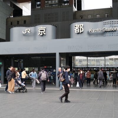 「JR」と「京都駅」の看板が掲げられた京都駅の入り口前は人々が行き交い、英会話マンツーマンの交流や、活気に満ちた街並みに浸るのに最適な賑やかな雰囲気を作り出しています。.