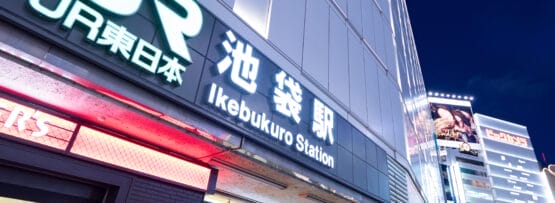 夜の池袋駅入口は、明るい看板の光の下、英会話マンツーマンなどのイベントを暗示する電飾看板が背景にあり、多くの人で賑わっています。.