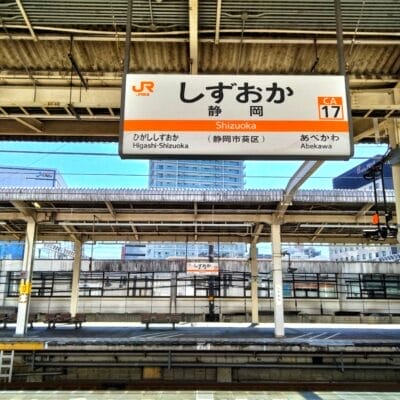 日本の静岡駅の空の電車のプラットフォーム。日本語の文字「静岡・三島」と駅の案内が書かれた看板が掲げられています。.