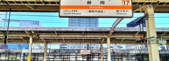 日本の静岡駅の空の電車のプラットフォーム。日本語の文字「静岡・三島」と駅の案内が書かれた看板が掲げられています。.