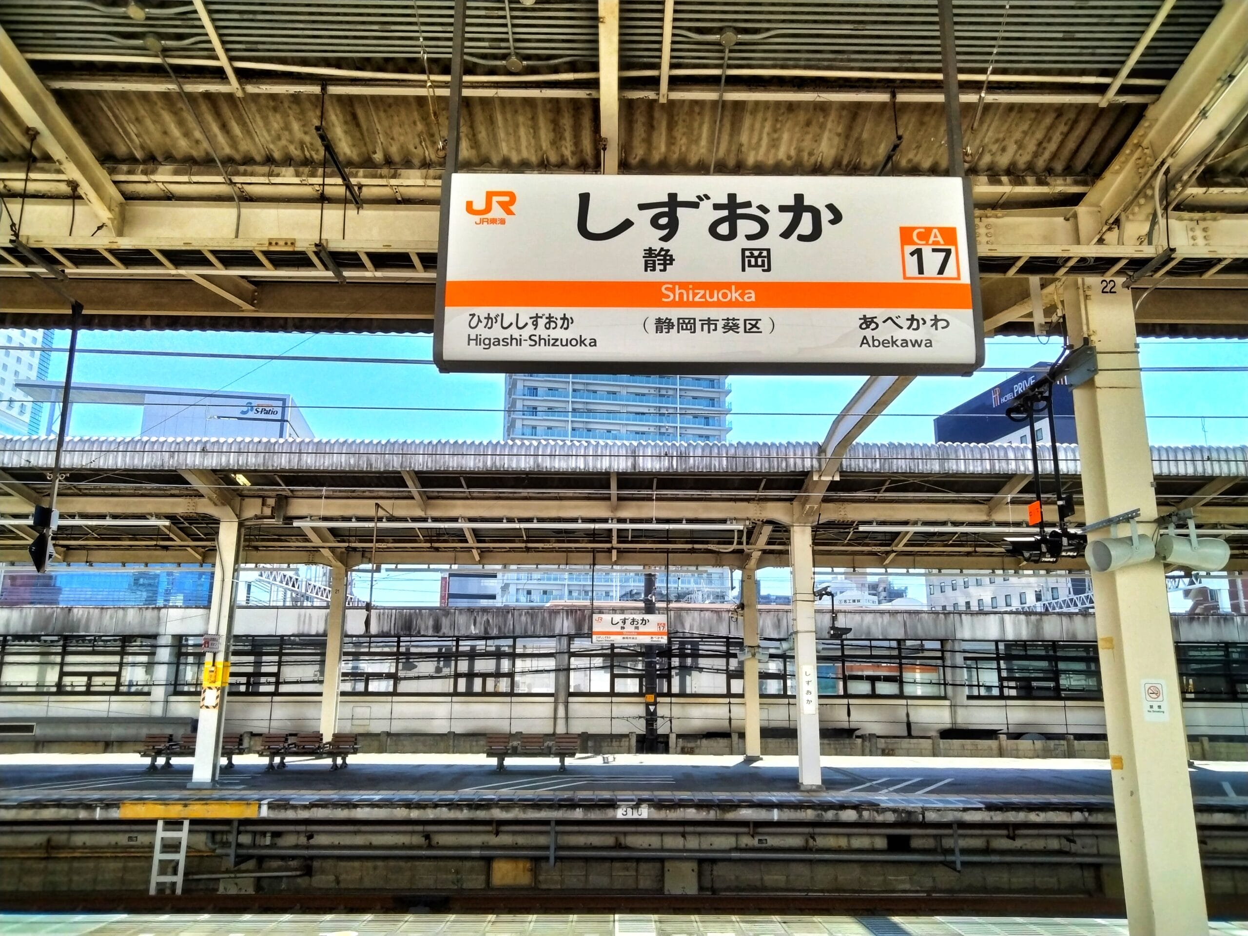 日本の静岡駅の空の電車のプラットフォーム。日本語の文字「静岡・三島」と駅の案内が書かれた看板が掲げられています。.