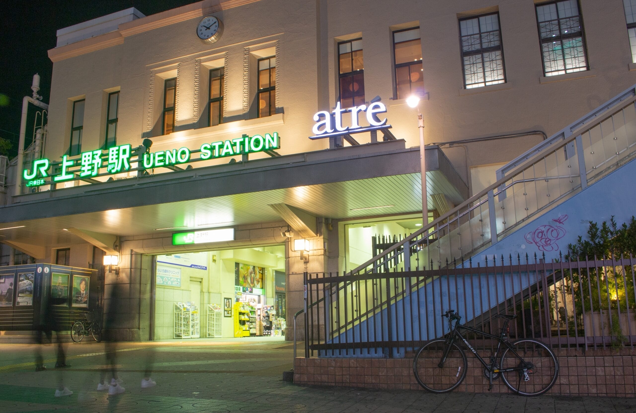 夜の上野駅の入り口は、ライトアップされた看板と隣接する建物が背景を鮮やかに彩ります。手前に駐輪された自転車が、上野の雰囲気を醸し出しています。.