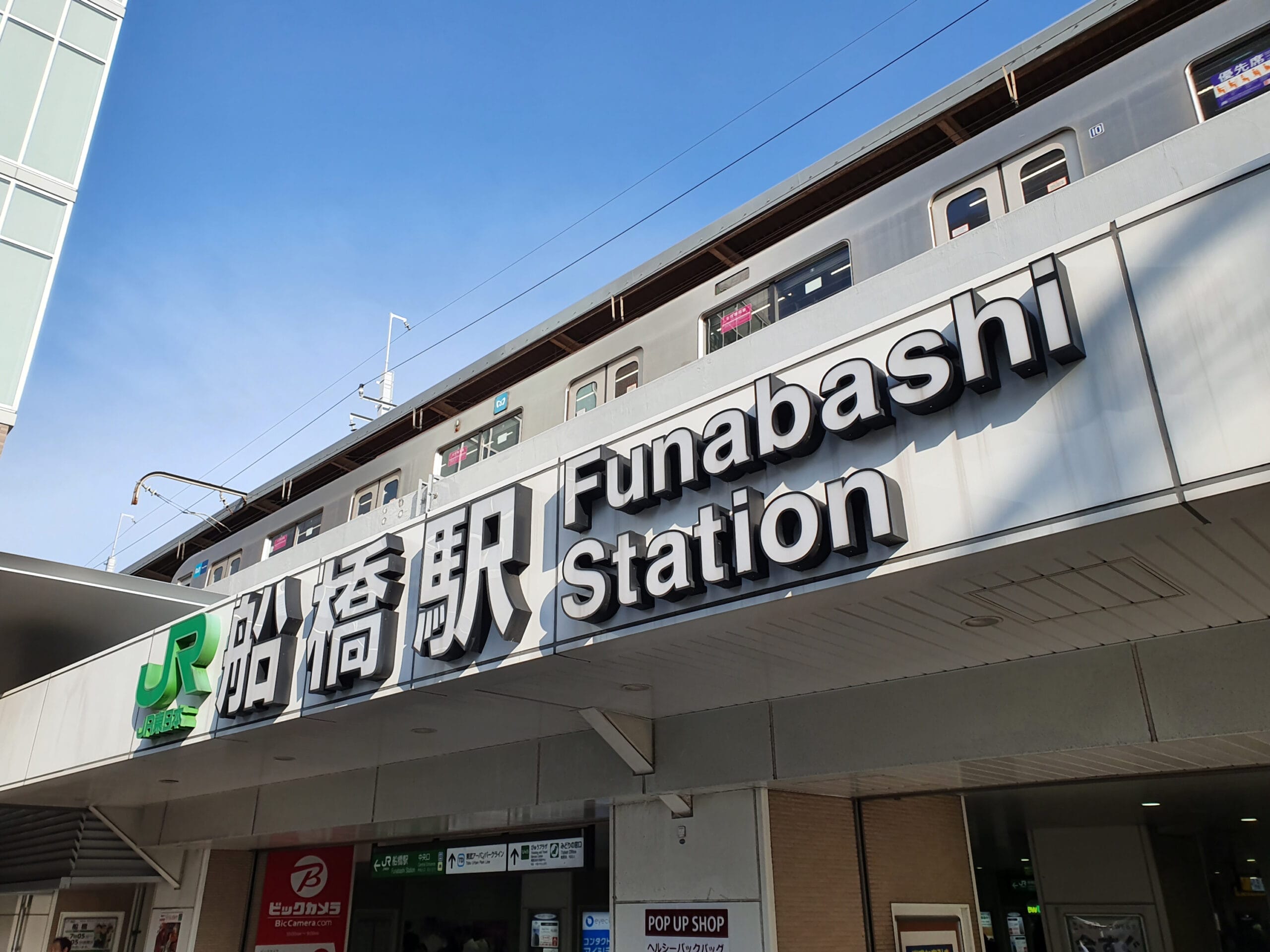 上に電車、下に店舗がある日本の船橋駅の看板。英会話マンツーマンのレッスンをお探しの方に最適です。.