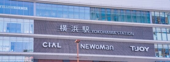 この画像は日本の横浜駅の外観を示しており、高層ビルのファサードに対してCIAL、NEWoMan、TJOYの看板が強調されています。活気あふれる横浜の街にあるこの賑やかなエリアは、文化的な楽しみを探索したり、近くで英会話マンツーマンのレッスンを見つけたりするのに理想的な場所です。.