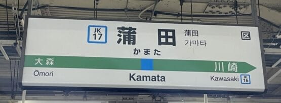 蒲田の駅標識には、英語、日本語、韓国語で「Kamata」と大森と川崎への行き先が表示されています。近くには、個人に合わせた言語学習を提供する英会話スクール マンツーマンがあります。.