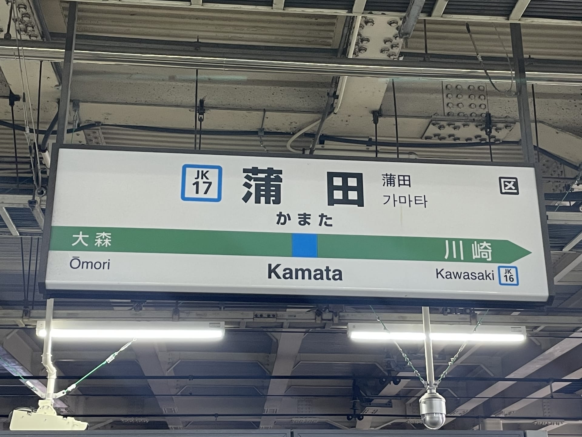 蒲田の駅標識には、英語、日本語、韓国語で「Kamata」と大森と川崎への行き先が表示されています。近くには、個人に合わせた言語学習を提供する英会話スクール マンツーマンがあります。.