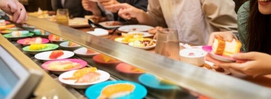 回転寿司屋に座って、さまざまな寿司の皿を選び、一緒に食事を楽しむ人々。.
